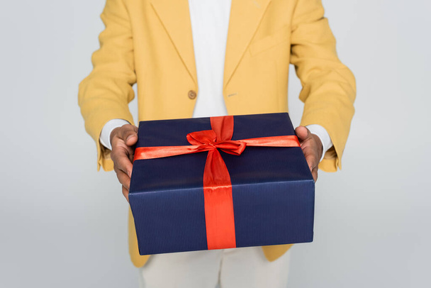 oříznutý pohled na afrického Američana ve žlutém stylovém blejzru držícím zabalený dárek izolovaný na šedi  - Fotografie, Obrázek