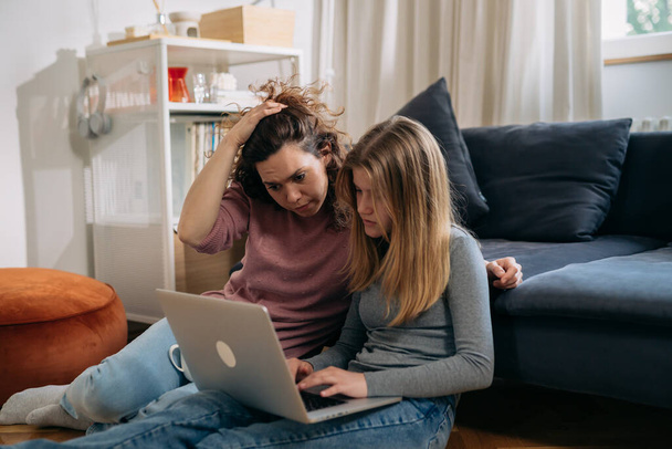 mother and daughter feeling relaxed sitting in living room and using laptop computer - 写真・画像