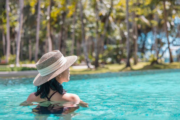 Šťastná Asiatka v červených plavkách a slaměný klobouk relaxující v bazénu s výhledem na bazén v Koh Mak, Phangnga, Thajsko. relaxovat a cestování koncept. Comfort resort letní dovolená. - Fotografie, Obrázek