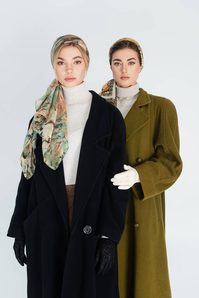 elegant women in headscarves and coats looking at camera isolated on grey - Foto, afbeelding
