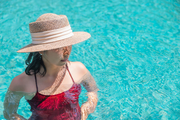 Happy asian woman in red swimsuit and a straw hat relaxing in swimming pool looking at view by the pool at Koh Mak, Phangnga, Thailand. relax and travel concept. Comfort resort summer vacation. - Photo, image