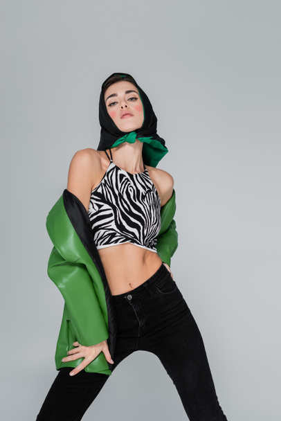 trendy woman in zebra print crop top and kerchief looking at camera isolated on grey - Foto, Imagem