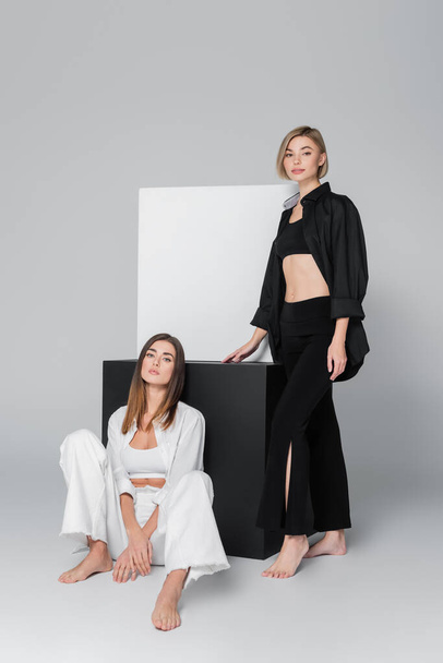 barefoot models in shirts and trousers posing near black and white cubes on grey background - Foto, afbeelding
