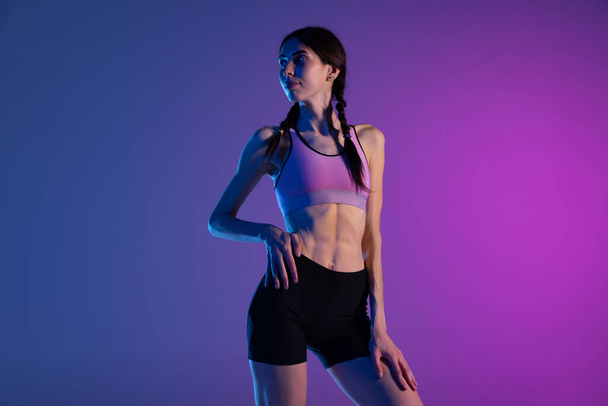 Beauty. Portrait of young fitness girl, female athlete in sports uniform posing isolated on pink blue background in neon. Sport, track-and-field athletics, competition concept. Copy space for ad, text - Foto, Imagem