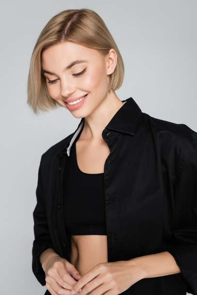 young blonde woman in black bra and shirt smiling isolated on grey - Photo, Image