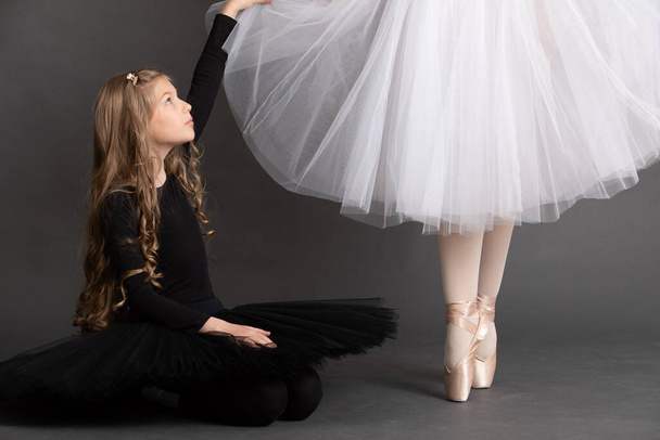 Mała dziewczynka siedząca blisko nóg baletnicy w baletnicach. - Zdjęcie, obraz