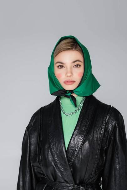 stylish woman in black leather jacket and green kerchief looking at camera isolated on grey - Фото, зображення