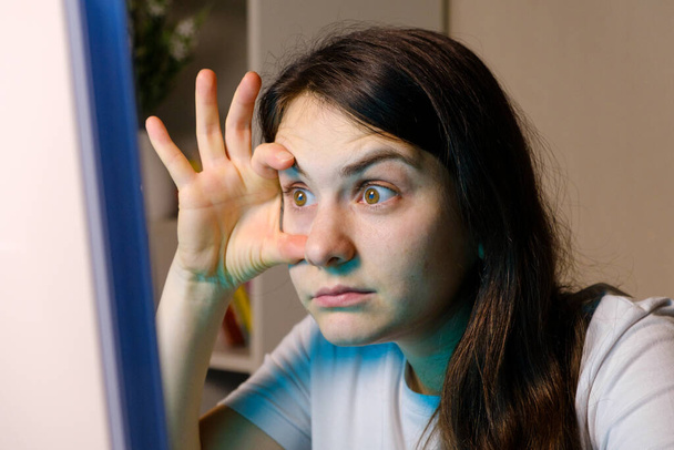 The woman forces herself to look into the computer screen, opening her eyes wide with her hands. - Photo, Image