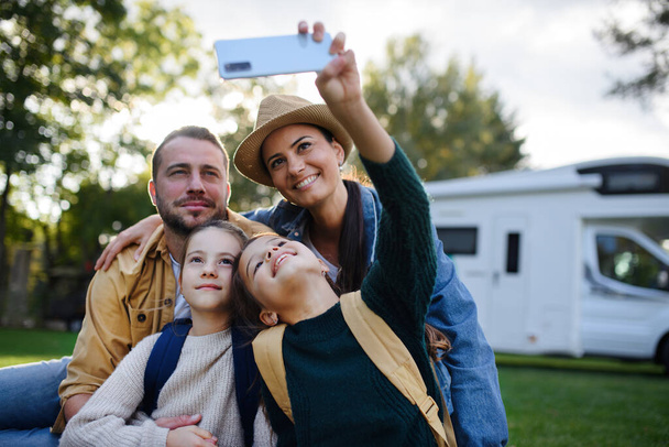 Una familia joven y feliz con dos niños tomando selfie con caravana al aire libre. - Foto, Imagen