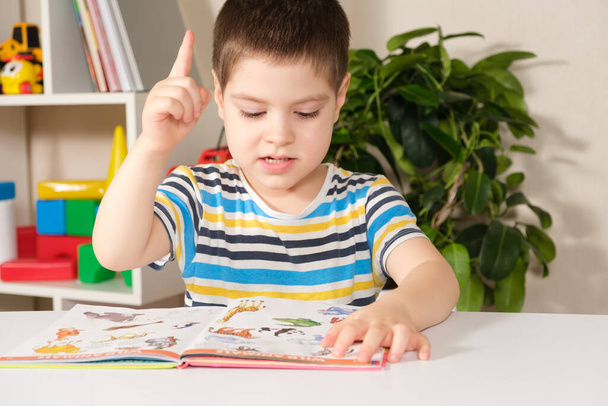 Egy 4 éves boldog fiú egy könyvet néz képekkel, képeket mutat és neveket ad nekik. - Fotó, kép