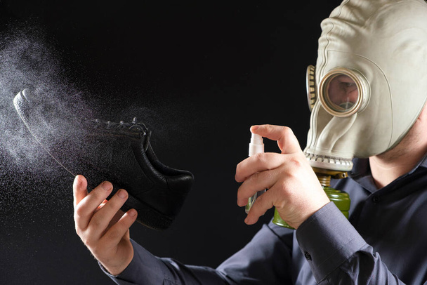 Ein Mann mit Gasmaske behandelt seine Schuhe mit einem Duftspray, das Problem des unangenehmen Geruchs von Füßen und Schuhen. - Foto, Bild