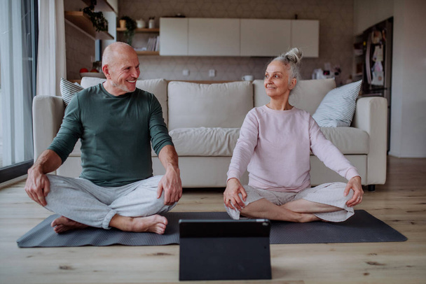 A senior couple doing relaxation exercise together at home. - Fotografie, Obrázek