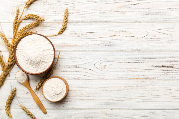 Επίπεδη στρώση σιτάλευρου σε ξύλινο μπολ με αγκάθια σιταριού σε χρωματιστό φόντο. παγκόσμια κρίση σίτου. - Φωτογραφία, εικόνα