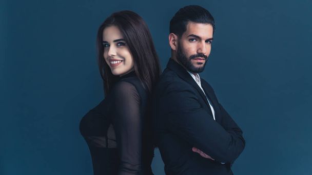 Interracial good-looking couple in their 30s dressed in elegant smart-casual clothes looking at camera and smiling. Studio shot, blue background. High quality photo - Foto, immagini