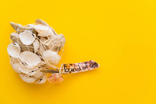 Top view of seashells in net with found at sea lettering on yellow background  - Foto, immagini