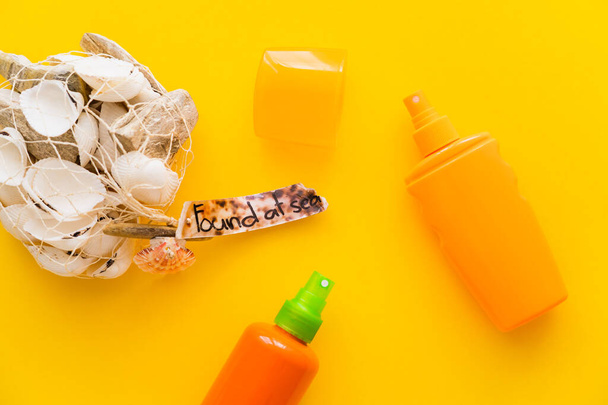 Top view of seashells with found at sea lettering near sunscreens on yellow background  - 写真・画像