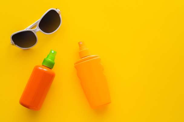 Top view of sunscreens near sunglasses on yellow background  - Fotoğraf, Görsel