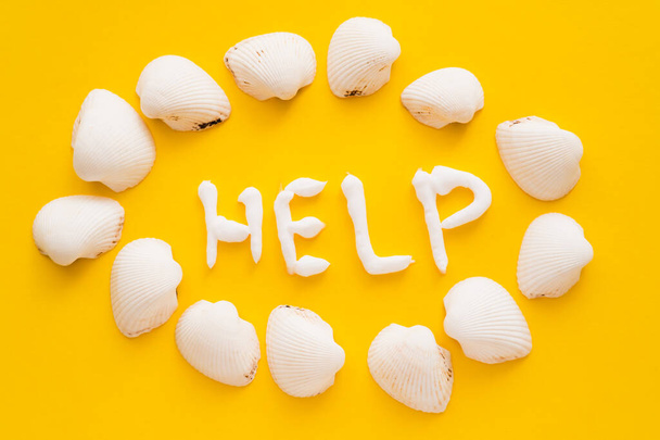 Top view of help lettering from sunscreen near seashells on yellow background  - Photo, Image
