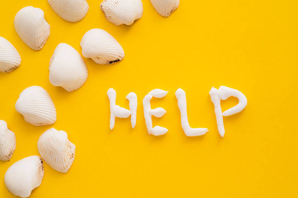 Top view of seashells and help lettering from sunscreen on yellow background  - Foto, imagen
