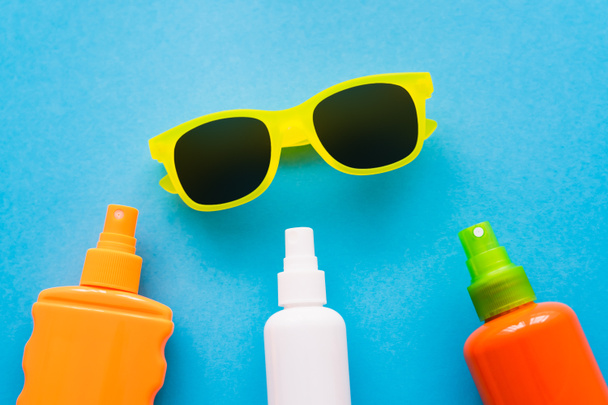 Top view of sunglasses near bottles of sunscreens on blue background  - 写真・画像