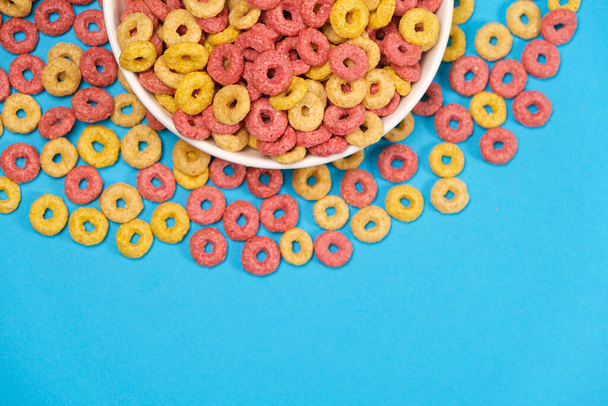 Corn rings of quick breakfast powder on a plate on a blue background, top view, place fot text. - Valokuva, kuva