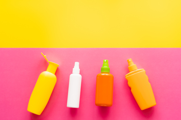 Top view of bottles of sunscreens on yellow and pink background  - Foto, Bild