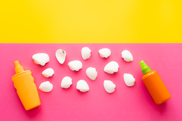 Top view of white seashells near sunscreens on yellow and pink background  - Foto, afbeelding