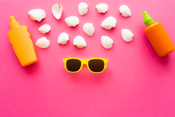 Top view of sunglasses near seashells and sunscreens on pink background  - 写真・画像