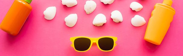 Vista dall'alto di occhiali da sole vicino a conchiglie bianche e creme solari su sfondo rosa, banner  - Foto, immagini