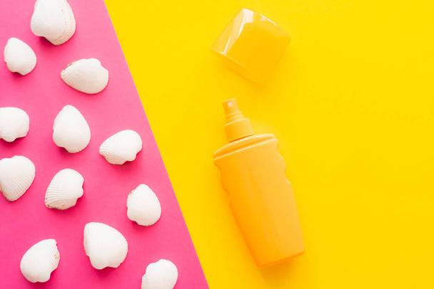Top view of seashells and sunblock on pink and yellow background  - 写真・画像