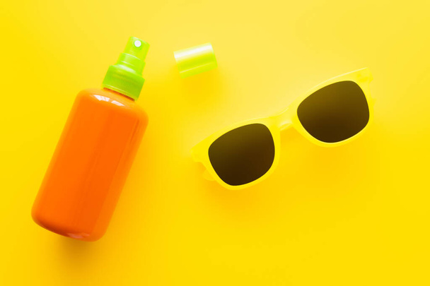 Κάτοψη αντηλιακού και γυαλιών ηλίου σε κίτρινη επιφάνεια  - Φωτογραφία, εικόνα