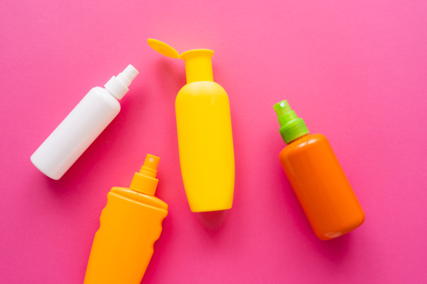 Draufsicht auf Flaschen mit Sonnenschutzmitteln auf rosa Oberfläche  - Foto, Bild
