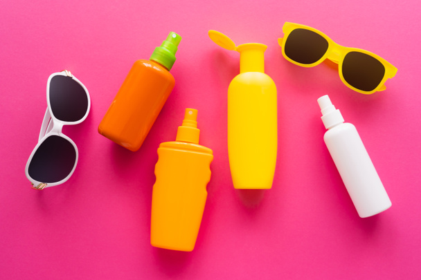 Bovenaanzicht van zonnebrillen en flessen zonnebrandcrème op roze oppervlak  - Foto, afbeelding