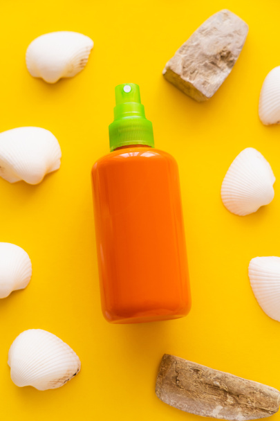 Top view of bottle of sunscreen near seashells and stones on yellow background  - Фото, изображение