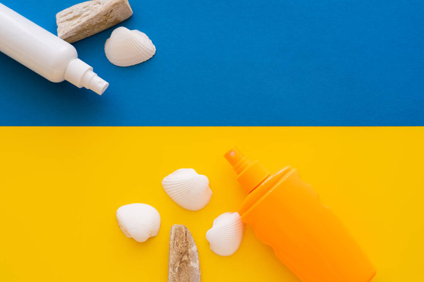 Top view of sunscreens near seashells and stones on yellow and blue background  - 写真・画像