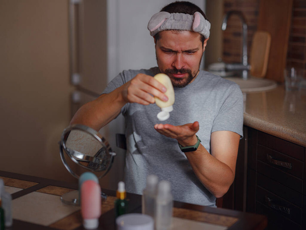 Miesten kauneuskäsite. Valkoihoinen mies tarkistamassa ihoaan. mies parta puristaa ulos ihonhoitotuotteet kerma, Miesten käsi kosteuttava voide, iho ja käsi hoito. - Valokuva, kuva