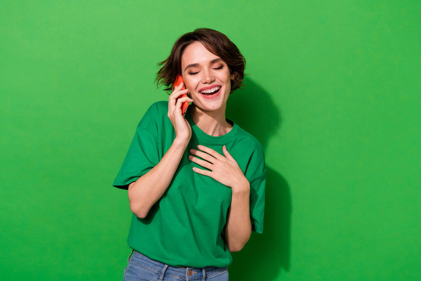 Fotografie zasněné funky žena nosit ležérní tričko komunikující moderní gadget izolované zelené barvy pozadí. - Fotografie, Obrázek