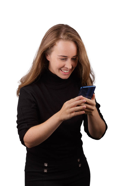 Young blonde girl smiling with mobile phone in hand wearing black jumper with white background - Fotoğraf, Görsel