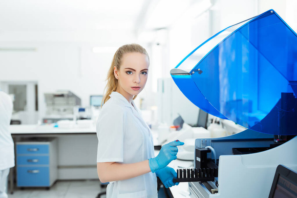 Ένας ιατρικός εργαζόμενος εργάζεται σε έναν αναλυτή αυτόματης Βιοχημείας και ανοσοποιητικού ενζύμου στο εργαστήριο της κλινικής - Φωτογραφία, εικόνα