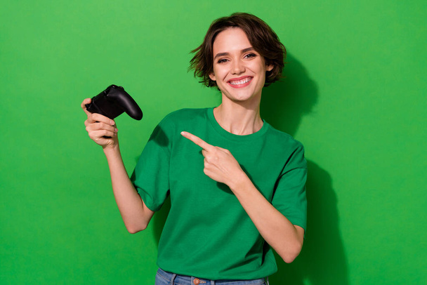 Photo of positive pretty person indicate finger game pad toothy smile isolated on green color background. - Фото, изображение