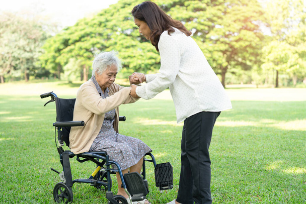 Pflegerin hilft und pflegt asiatische Seniorin oder ältere Dame Patientin im Rollstuhl sitzend und glücklich im Park, gesundes starkes medizinisches Konzept. - Foto, Bild