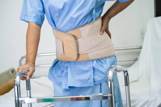 Asiática señora paciente usando espalda dolor soporte cinturón para ortopédica lumbar con walker. - Foto, Imagen