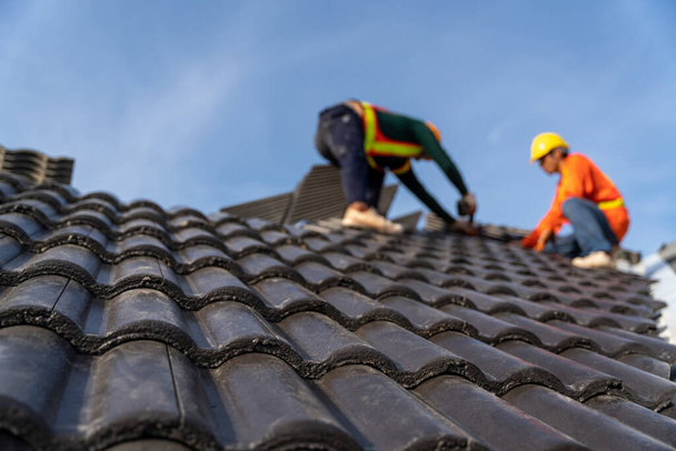 2 dakdekkers werken aan de werkzaamheden op hoogte om de betonnen dakpannen te installeren op het nieuwe dak van nieuwe moderne gebouwenbouw. Selectieve focus van Beton dakpannen. - Foto, afbeelding