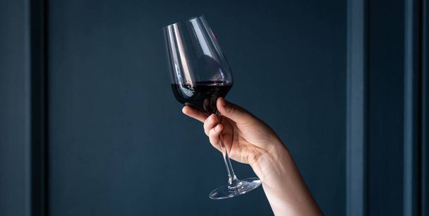 A glass of red wine in a female hand on a blue background isolated. - 写真・画像