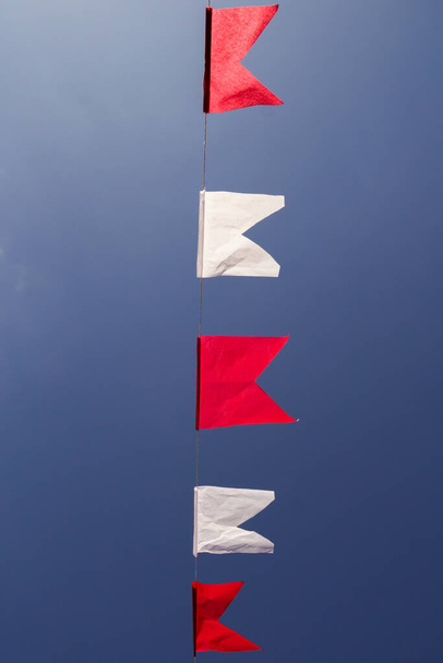  Una línea de banderas en blanco y rojo, colgando con el cielo azul en el fondo. - Foto, Imagen