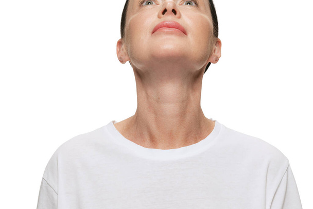 Cropped portrait of happy middle age beautiful woman with well-kept skin looking up on white background. Cosmetics, spa, age-related changes, face lifting and skin care concept - Zdjęcie, obraz