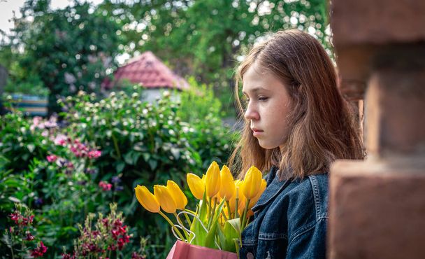 Little girl with a bouquet of yellow tulips in a pink paper bag. - Photo, image