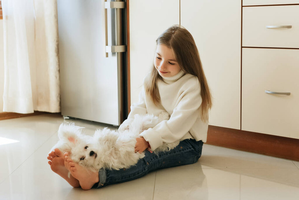 dziewczyna 9 lat z długie włosy model z pies maltański uczennica w domu styl życia na beżowy tło alergia weterynarz - Zdjęcie, obraz