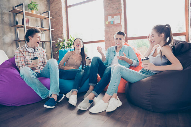 Photo of funny funky workers group sitting dorm bean bags drinking beverages laughing indoors workplace workshop. - 写真・画像