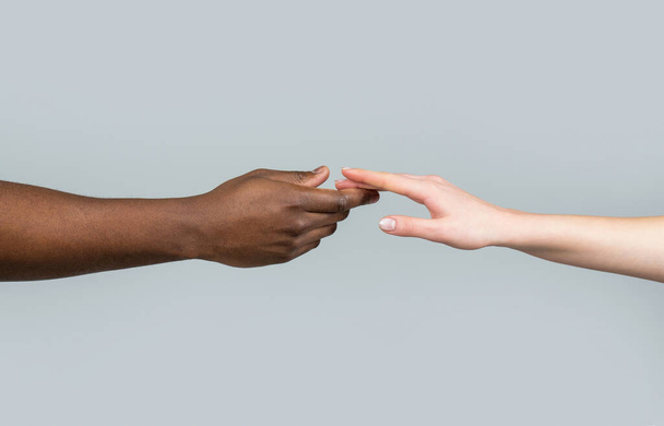 Hand skin colors touch two. Woman and African American man touching hands. White Caucasian female hands and black African American holding fingers together. World unity and racial love and races. - Fotó, kép